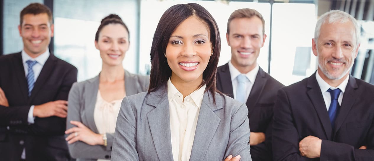 (direct upload) A confident woman stands in front with a group of four smiling professionals, all dressed in business attire, posing in an office setting.
