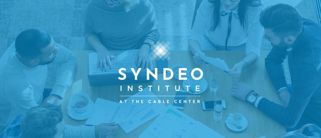 Five people sit around a table with laptops and documents, under the Syndeo Institute at The Cable Center logo.