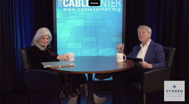 Ann Carlsen and Stewart Schley sit at a round table with mugs and a laptop, engaging in cable oral history interview in a studio with "The Cable Center" display in the background.